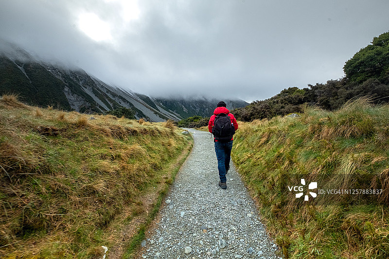 在新西兰库克山国家公园胡克谷步道上行走的一名男子，背景是云雾缭绕的山脉图片素材