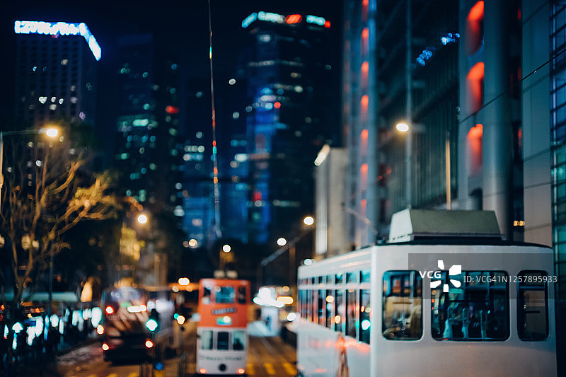 香港繁忙的夜生活：公共交通和有轨电车在市区道路上行驶，背景是灯火通明的现代企业摩天大楼图片素材