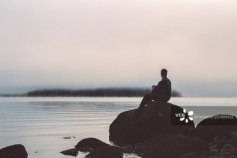 在雾蒙蒙的湖边岩石上坐着的男人剪影图片素材