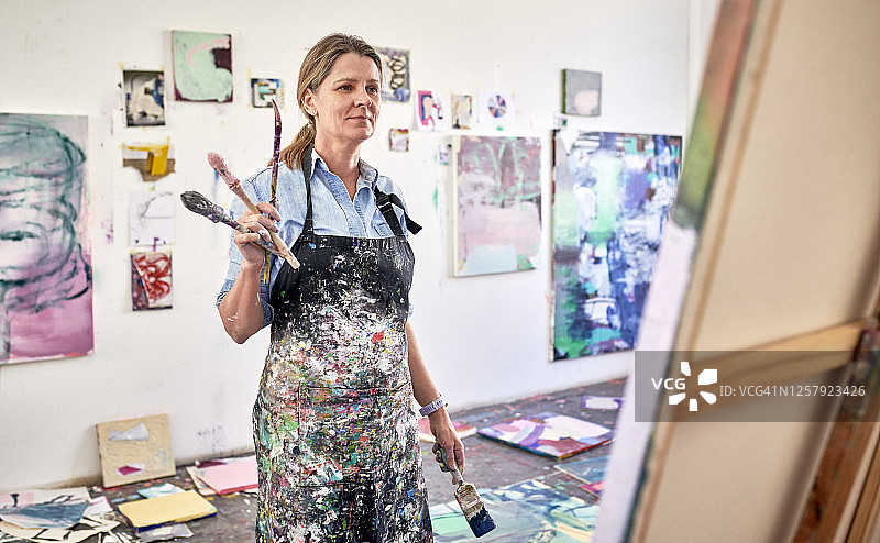 女艺术家在工作室的肖像：站在画布前工作图片素材