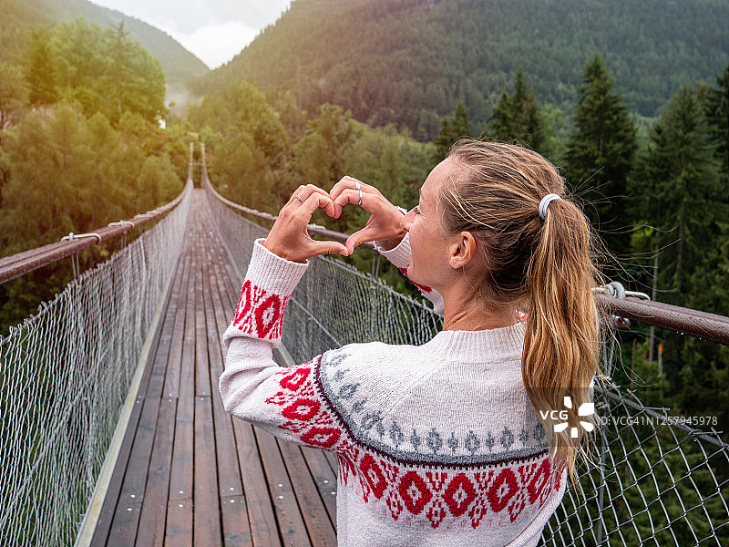 女人在松树林上方的吊桥上用手比心图片素材