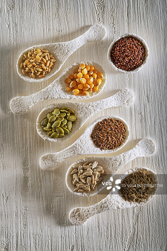 白色背景下勺子中的藜麦亚麻籽香芹籽颗粒配料图片素材