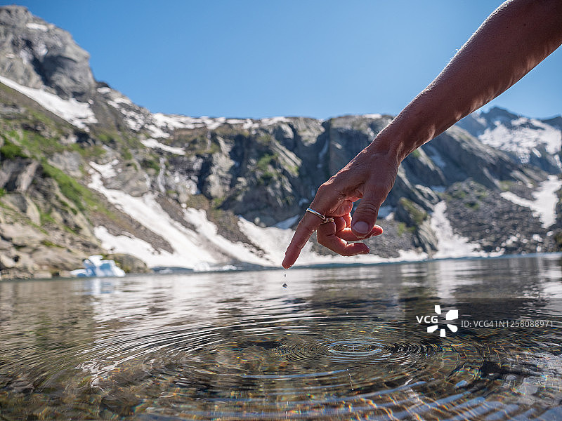 女人的手指触碰高山湖泊水面图片素材