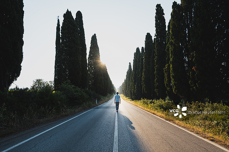 在意大利排列着柏树的笔直道路上行走的男人图片素材