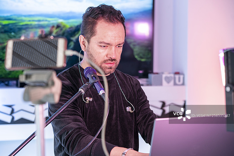 男人在笔记本电脑上进行电话会议并用游戏机播放音乐。图片素材