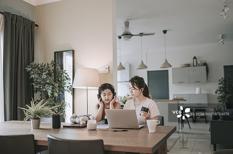 一位在餐厅使用笔记本电脑工作的中年亚洲女性，女儿陪伴在她身边图片素材