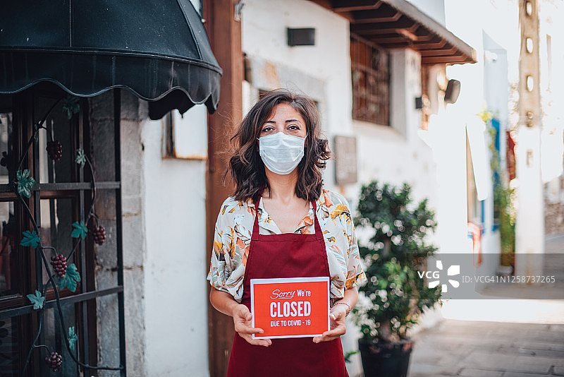 疫情后小商店里女人手持暂停营业标志图片素材