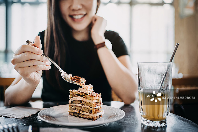 年轻亚洲女人在咖啡馆享受蛋糕和冰茶图片素材