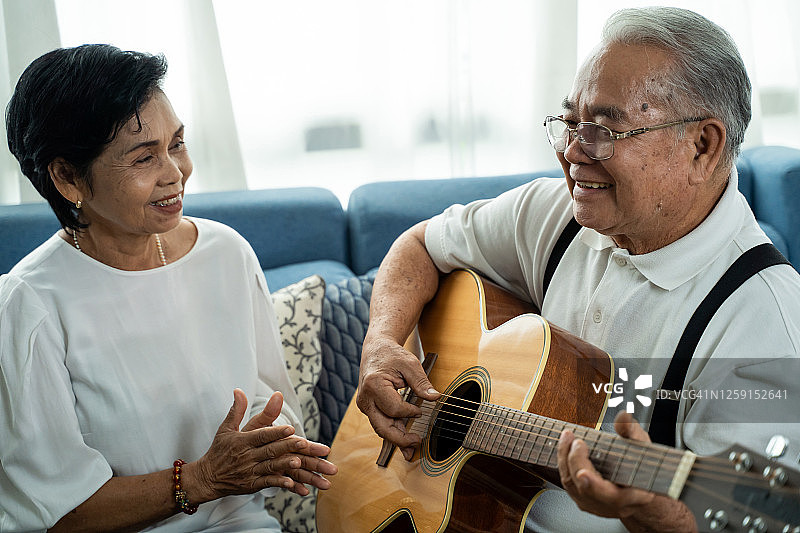 亚洲老年夫妇坐在沙发上一起弹吉他图片素材