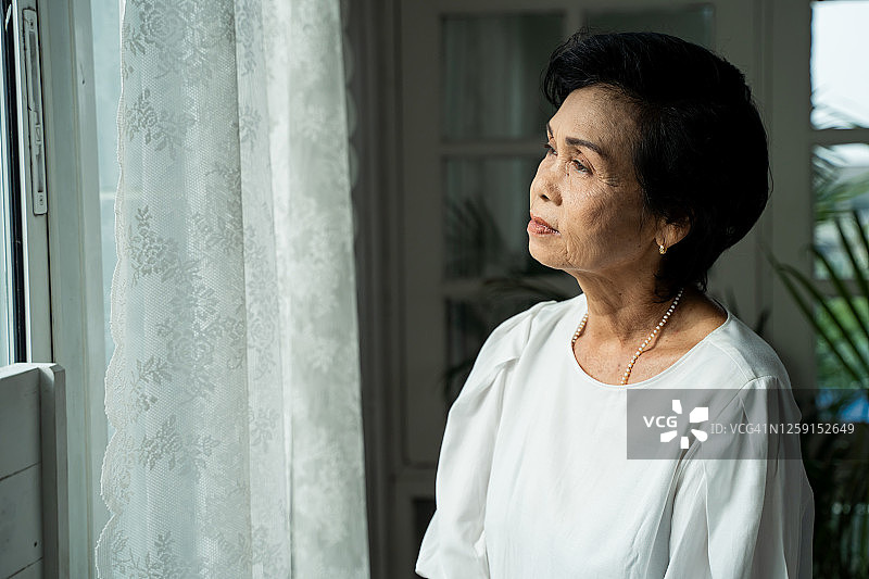 若有所思的老妇人望着窗外，感到孤独的特写。70多岁的亚洲老年女性养老金领取者想念孩子和丈夫图片素材