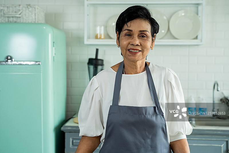 快乐的年长亚洲女性在家中厨房准备午餐，面带微笑，双臂交叉图片素材