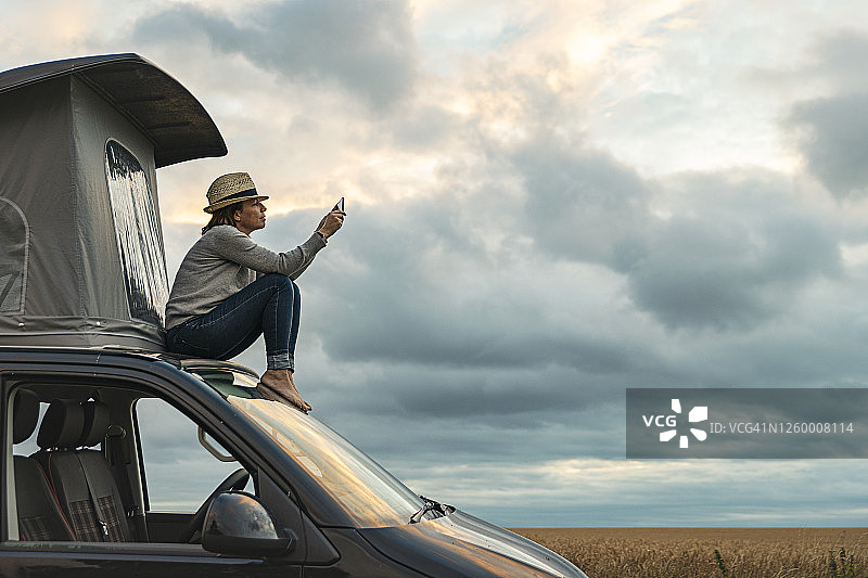 日落时分，女人坐在露营车顶上拍照图片素材