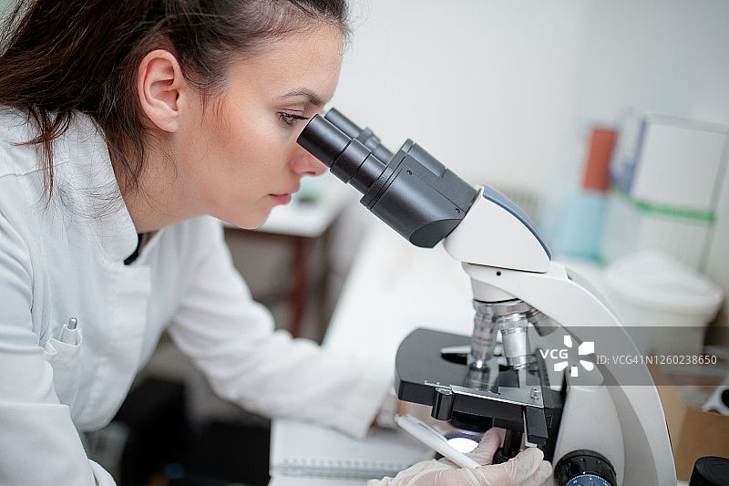 戴着防护手套的女微生物学家正在用显微镜观察图片素材