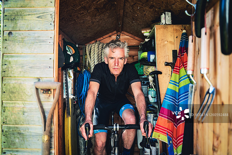 在棚子里独自骑自行车的表情严肃的男人图片素材