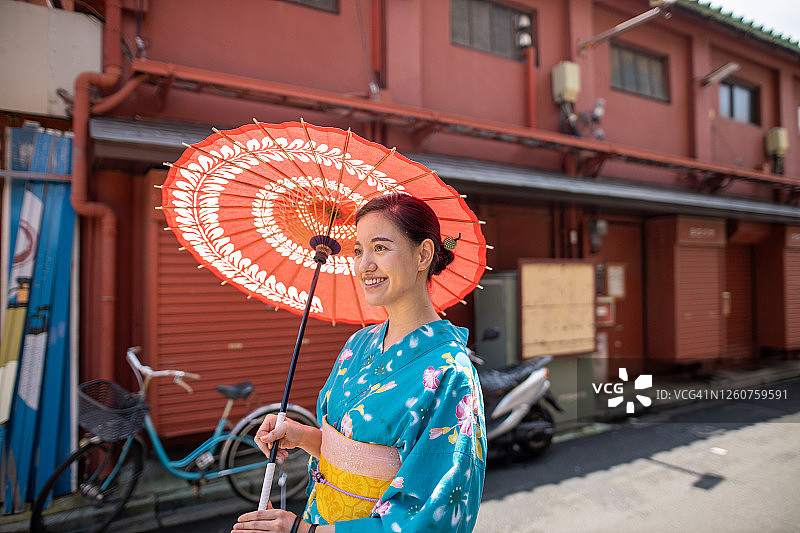 身穿浴衣的年轻女人拿着纸伞走在日本传统街道上图片素材