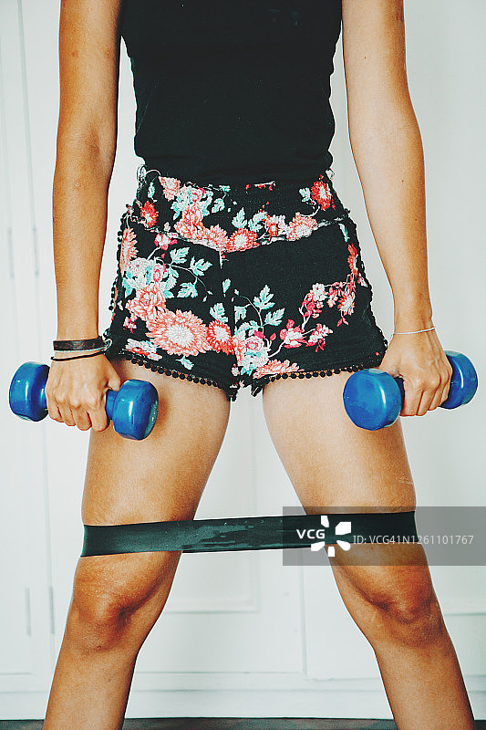 穿着运动服在家用哑铃和弹力带锻炼的年轻女人图片素材