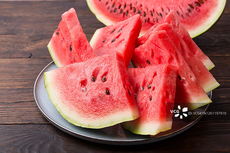 木桌背景上切开的西瓜片，多汁的红色瓜瓤图片素材