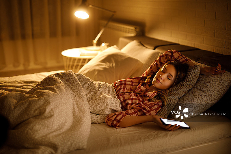 年轻女人在床上睡着了，手里拿着手机图片素材