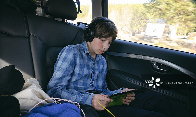 男孩坐在车里戴着耳机拿着数码平板，位于瑞典韦斯特博滕省图片素材