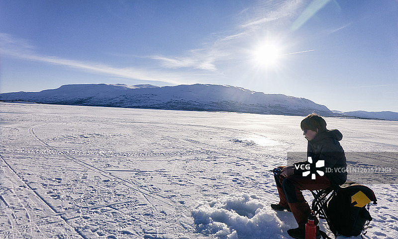 男孩在瑞典西博滕省冰冻的湖面上冰钓图片素材