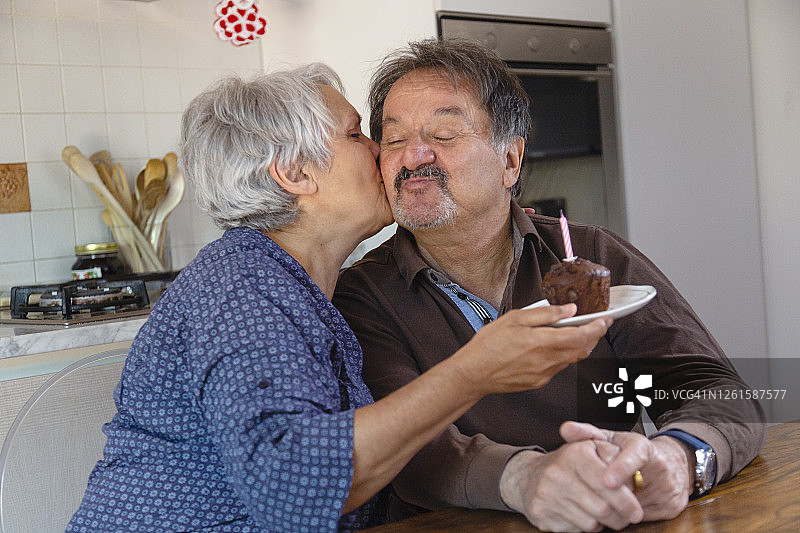 老年夫妇手捧生日蛋糕，亲吻，在疫情隔离期间进行在线庆祝图片素材