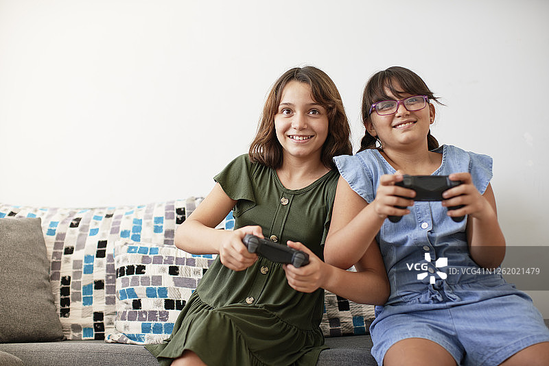 坐在沙发上玩电子游戏的两个女孩图片素材