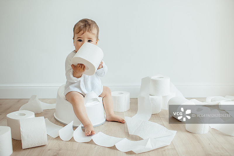 可爱的女宝宝坐在白色便盆上玩卫生纸图片素材