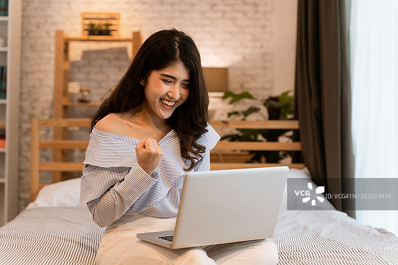 用笔记本电脑庆祝成功的快乐亚洲女士图片素材
