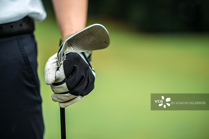 亚洲年轻男子高尔夫球手手持高尔夫球杆在球场上的特写图片素材