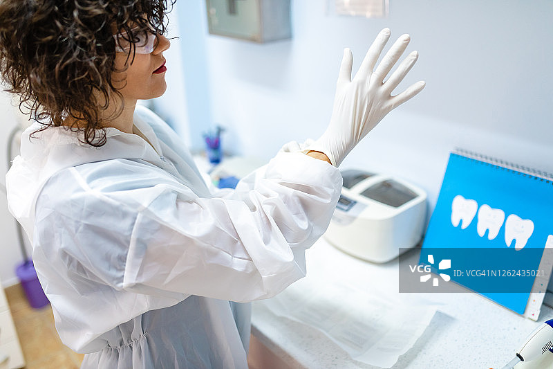 有责任心的女牙医戴上无菌外科手套，保护自己和病人免受冠状病毒侵害图片素材