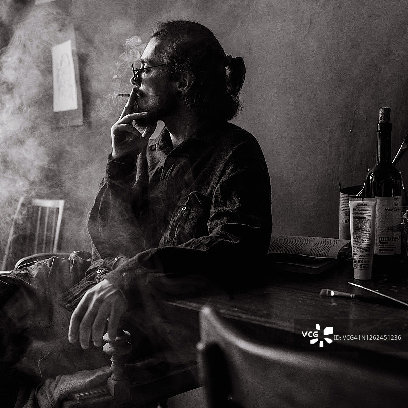 年轻艺术家坐在凌乱的工作室里抽烟图片素材