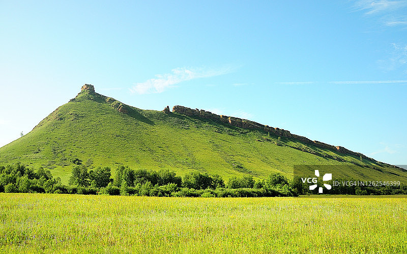 长满草和灌木的高山，顶部有一块矩形石头图片素材