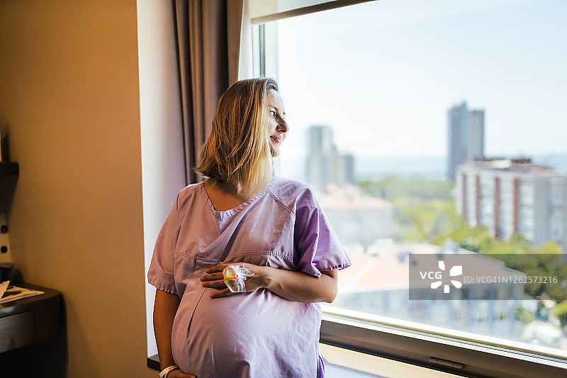 年轻孕妇在医院病房的窗边抚摸着肚子，等待分娩图片素材