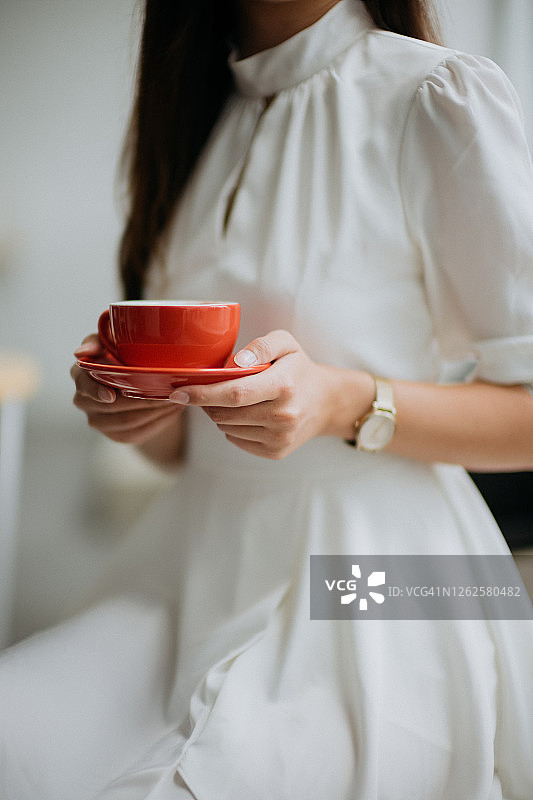 年轻亚裔女性手持红色咖啡杯和茶托图片素材