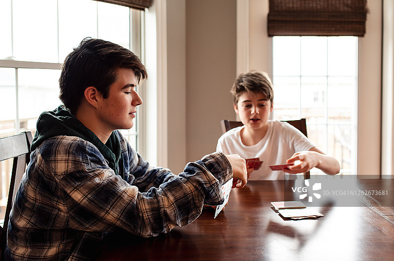 两个青少年男孩在厨房的餐桌旁玩牌图片素材