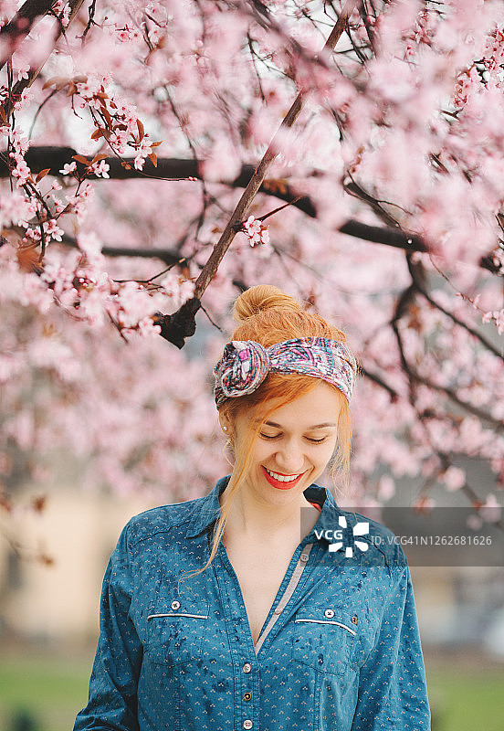 年轻女子站在春天的花树下，淋着雨图片素材