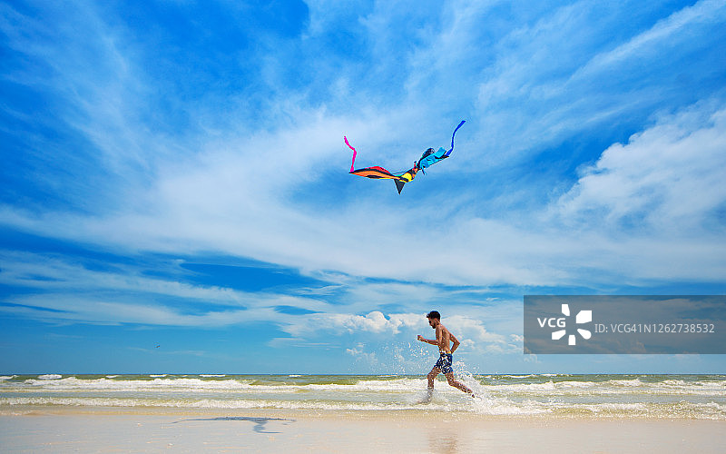 年轻男人在空旷沙滩上放风筝图片素材