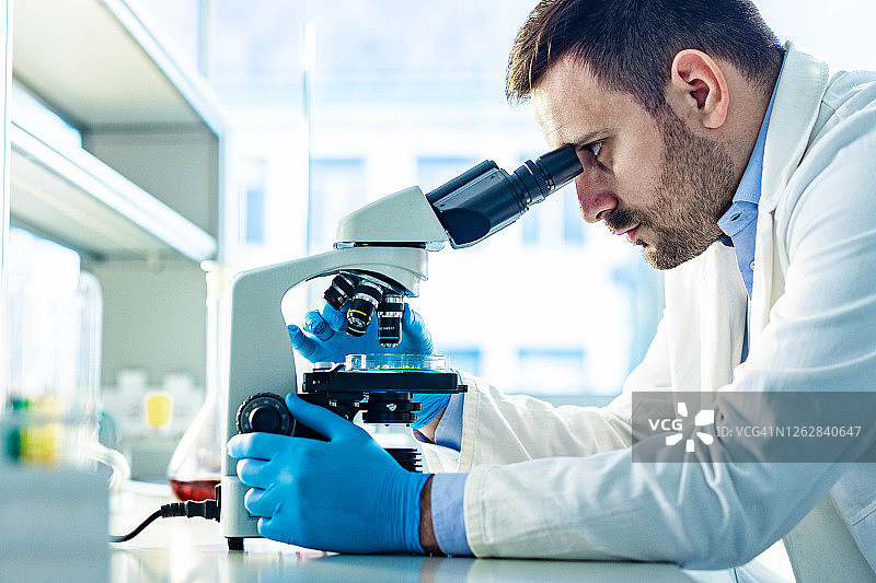 年轻男科学家在实验室用显微镜工作图片素材