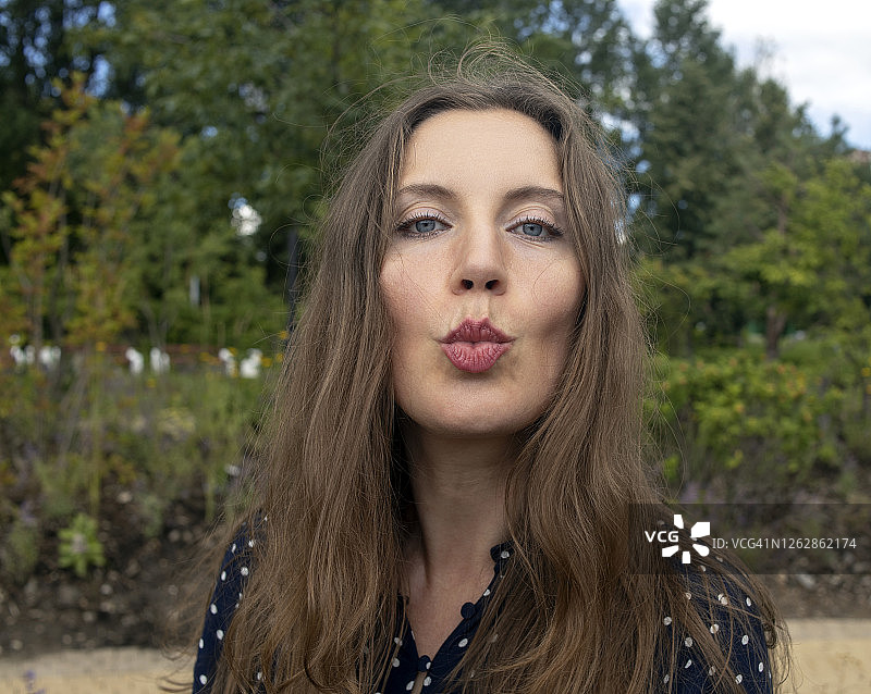 公园自然背景下，发送飞吻的年轻迷人黑发丰唇女子户外肖像图片素材