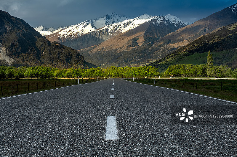 新西兰南岛格莱诺基附近：雪山和树木背景下的笔直空旷道路图片素材