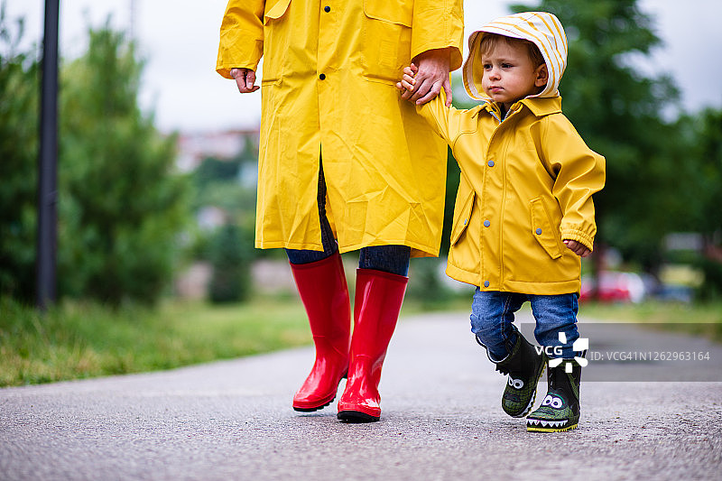母亲和幼儿穿着雨靴和雨衣在雨中玩耍图片素材