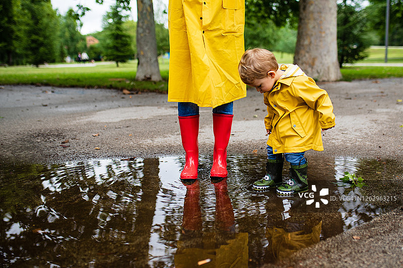 母亲和幼儿穿着雨靴和雨衣在雨中玩耍图片素材