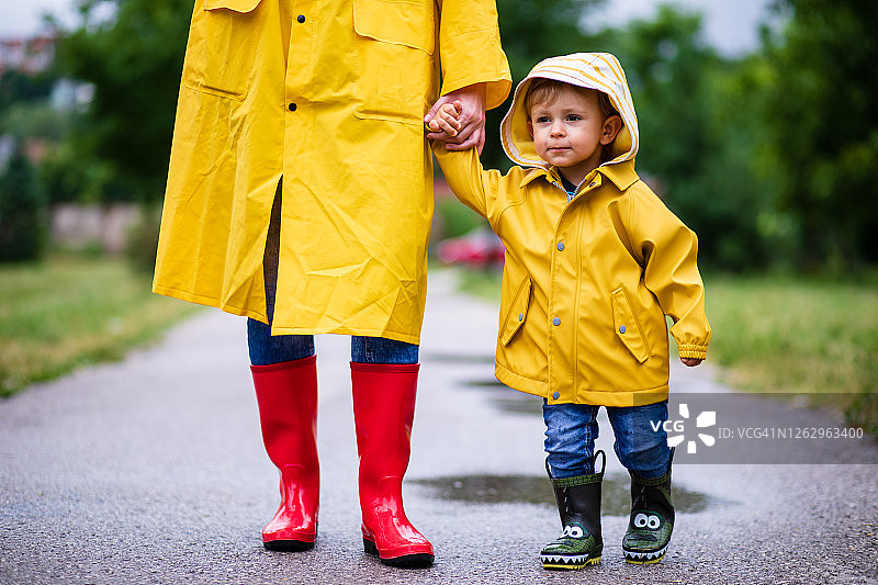 母亲和幼儿穿着雨靴和雨衣在雨中玩耍图片素材