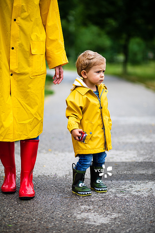 母亲和幼儿穿着雨靴和雨衣在雨中玩耍图片素材