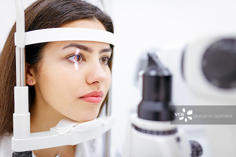 年轻女人靠在光学仪器上进行眼科检查图片素材