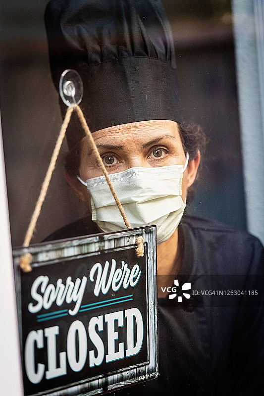 表情严肃的女厨师在餐厅橱窗前看关门告示图片素材