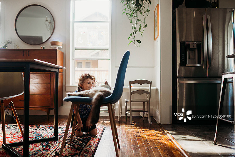 坐在餐厅地板上与宠物猫玩耍的学龄前女孩图片素材