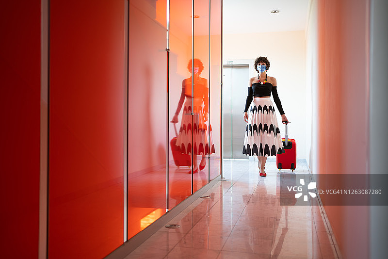 带着行李，戴着防护口罩进入酒店的女人。她正穿过空旷的走廊走向她的房间。图片素材