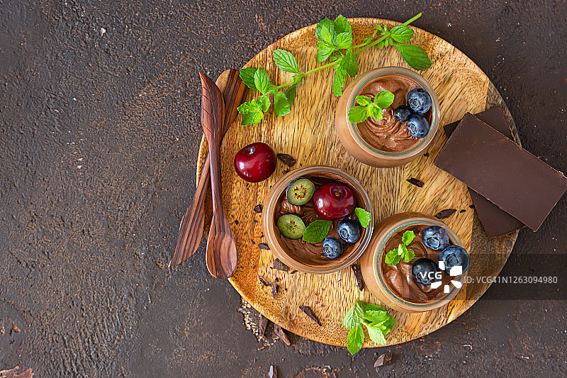 巧克力慕斯或布丁，用甜樱桃、蓝莓、薄荷和巧克力片装饰的份量罐子。选择性聚焦。乡村风格。深色背景。图片素材