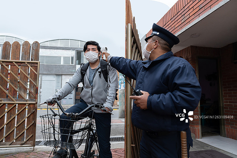 保安使用红外线温度计测量门口送货员的体温图片素材